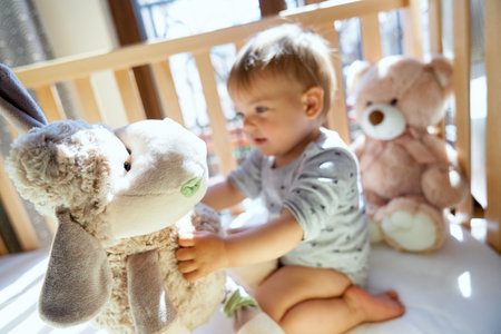 Smiling little child sitting on a wooden bed and holding a large plush sheepの写真素材