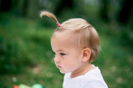 Little girl with a ponytail on a green meadow. Portrait. Side viewの写真素材