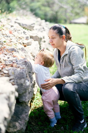 Mom sat down next to a little girl near stones in a green parkの写真素材