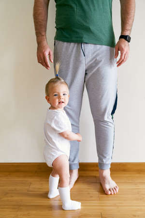 Little girl stands and holds on to daddys leg in the roomの写真素材
