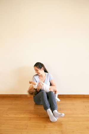 Smiling mom sitting on the floor and holding a little girl in her armsの写真素材