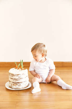 Little girl sitting on the floor in the room and looking at the carrot cakeの写真素材