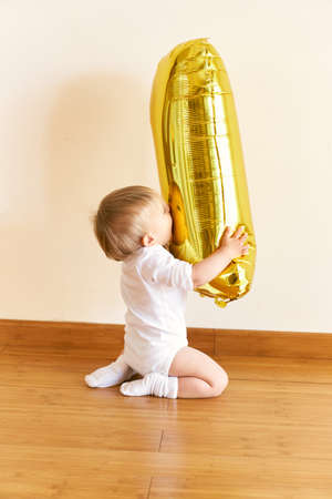 Little girl sits on her knees and holds an inflatable number one in her hands
