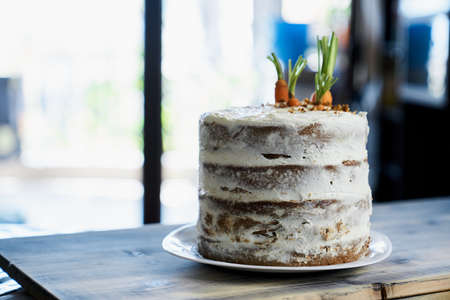 Carrot cake stands on a white plate on the table against the background of the window