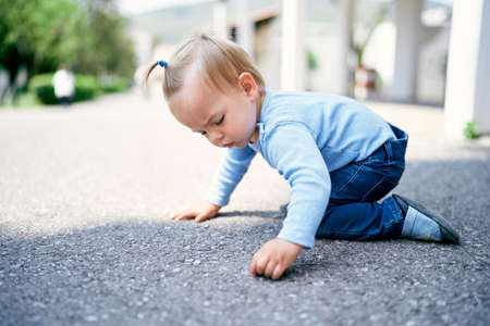 Little girl with a ponytail sits on her knees on the road in the parkの写真素材