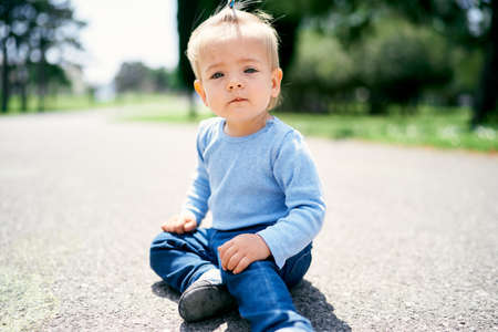 Little girl with a ponytail sits on the road in the parkの写真素材