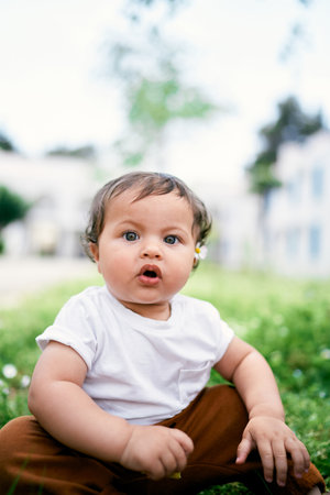 Little girl with chamomile behind her ear sits on green grassの写真素材