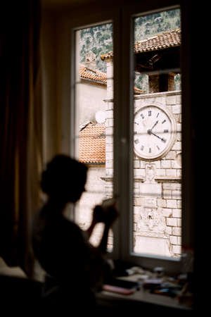 Silhouette of the bride standing by the window in a hotel room before the wedding ceremony. Clock tower in the windowの写真素材