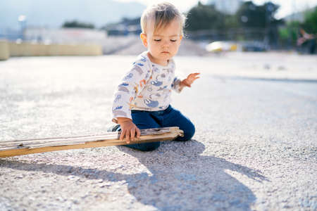 Cute kid sits on the beach and holds a stick in his handの写真素材