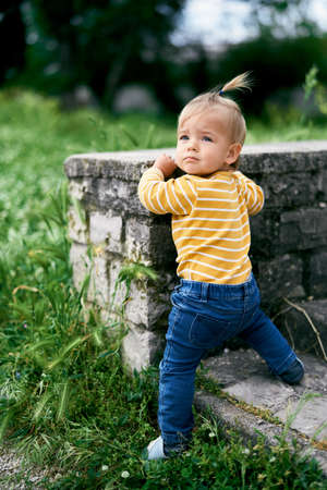 Little girl stands at a stone fence in the park, turning her head