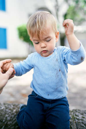 Kid sits on a stone fence in the yard with his hands up