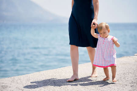Mom leads a little girl by the hand along a concrete breakwater