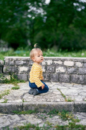 Little girl sits on her knees on stone steps in the park