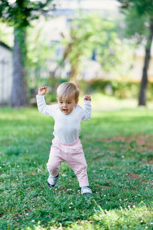 Kid walks on a green lawn with wildflowers raising his fistsの写真素材