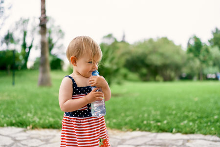 Little girl hugs a bottle of water while standing on a path in the parkの写真素材