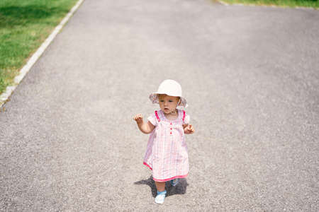 Little girl in dress and hat walks on the asphaltの写真素材