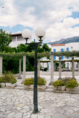 Lantern against the backdrop of a green patio, a house and bushes in tubs