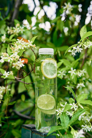 Bottle of water with slices of lemon and lime inside stands on a post near a flowering tree