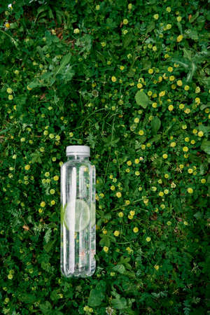 Water bottle with lime lies on green grass among yellow wildflowersの写真素材