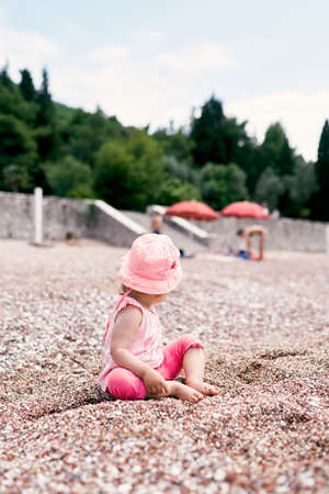 Little girl in panama sits on the beach, turning backの写真素材