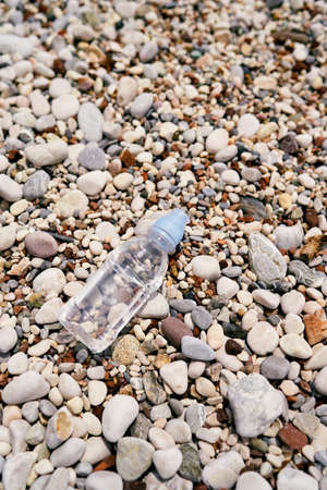 Small bottle of water lies on a pebble beach. View from above