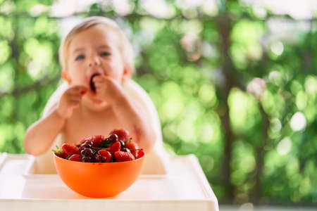 Bowl of fruit on a table on the balcony in front of a eating child