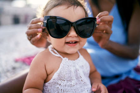 Mom puts big sunglasses on an enthusiastic little girl