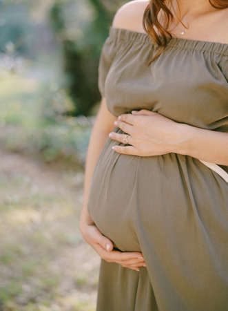 Pregnant woman in green dress supports belly with hands