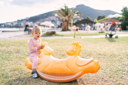 Kid sits on a swing on the beach against the backdrop of mountains and green treesの写真素材