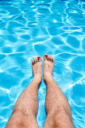 Male feet over blue water in a pool under the sun. Close-upの写真素材