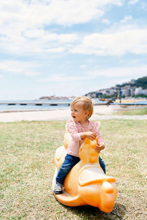 Little child sits on a swing in the playground by the seaの写真素材