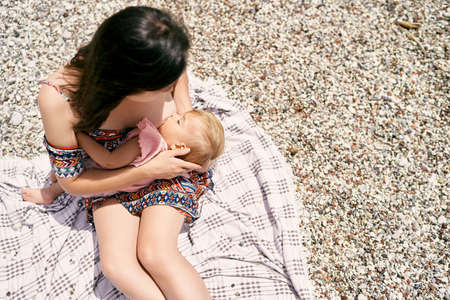 Mom is breastfeeding a little girl on a pebble beach. Top view