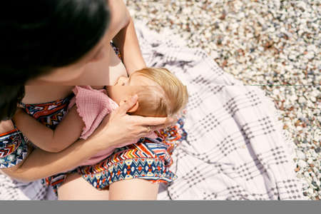 Mom breastfeeds a little girl on a pebble beach. Top view. Close-upの写真素材