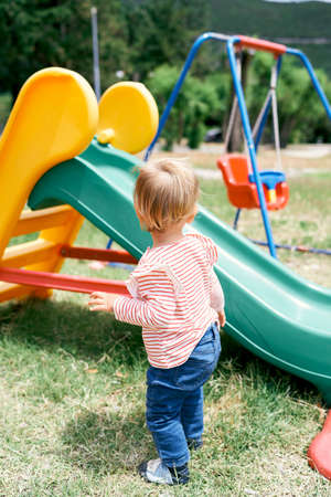 Little girl stands near the children slide in the playgroundの写真素材