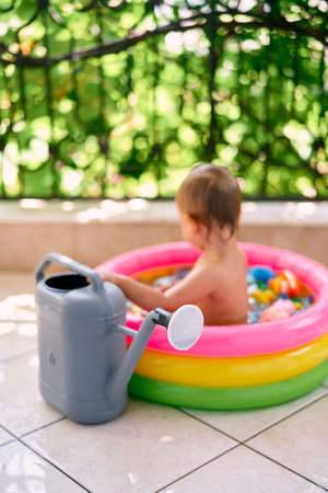 Big garden watering can stands against the background of a toddler sitting in an inflatable...