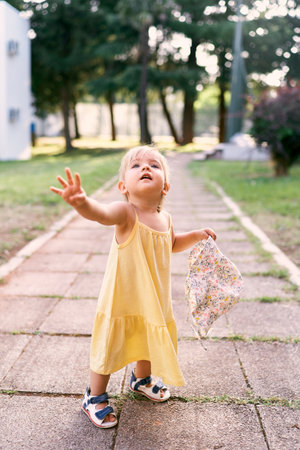 Little girl with a panama hat in her hand looks up, standing on a cobbled walkwayの写真素材