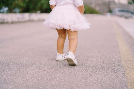 Legs of a little girl in a fluffy skirt stand on the asphalt road