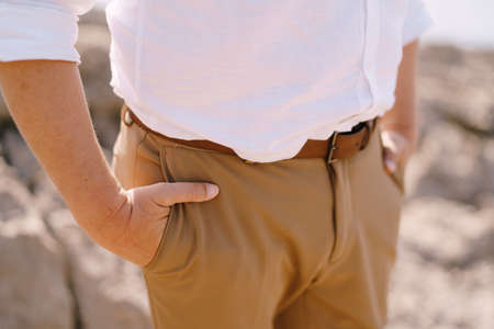 Man holds his hands in his trouser pockets while standing on a rock. Close-upの写真素材