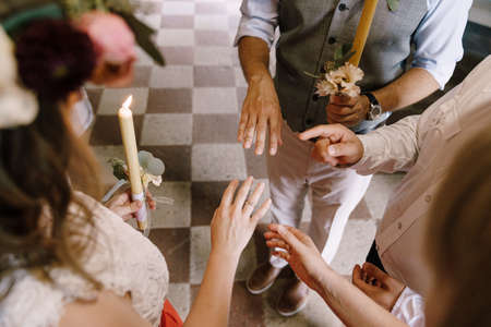 Priest stands near groom and bride with a ring on her finger and candles in their handsの写真素材