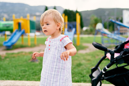 Little girl stands on the playground against the background of slidesの写真素材