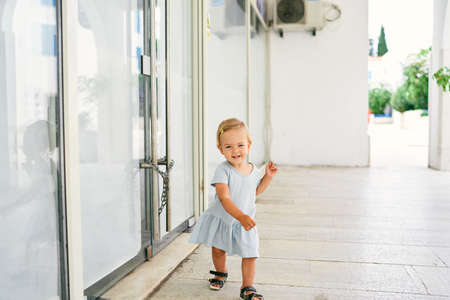 Little smiling girl walking on the tiles near the glass door of the houseの写真素材