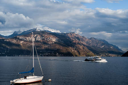 Pleasure ship sails past the pier against the backdrop of mountains. Lake Como, Italy