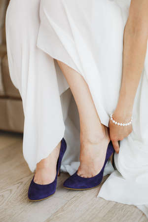 Bride in a white dress with a pearl bracelet on her arm wears blue high-heeled shoes on her feet. Close-upの写真素材