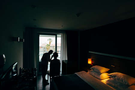 Make up artist does make up to a client by an open window in the bedroom. Twilight in the roomの写真素材