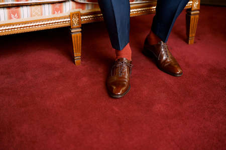 Legs of a man in blue pants, red socks and brown shoes sitting on a sofa in the hotel room, close-upの写真素材