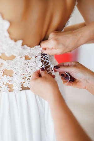 Womens hands lace up the lace corset of the brides wedding dress. Close-up
