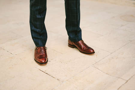 Man in black plaid trousers and brown patent leather shoes stands on a tile floor. Legs close upの写真素材