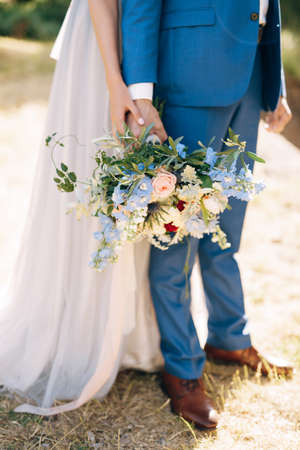 Groom in a blue suit holds a bouquet of flowers in his hand. Bride in a white dress hugs him from behind. Close-upの写真素材