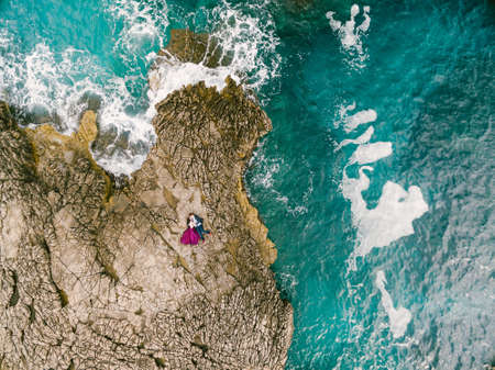 Man and woman lie embracing on the rocks by the blue foaming sea. View from above