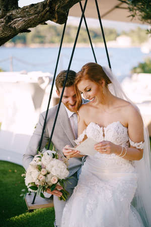 Bride and groom sit on a swing and read a postcardの写真素材